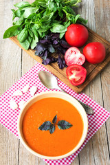 Fresh tomato soup with basil and tomatoes on wooden table
