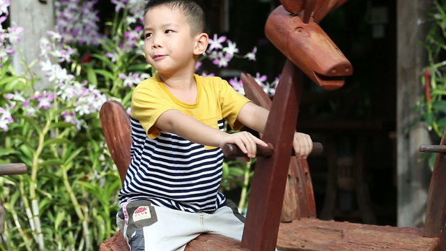 asian kid playing on the wooden rocking Horse