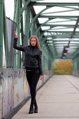 Obraz premium Beautiful blonde woman in leather jacket and leggings on a bridge
