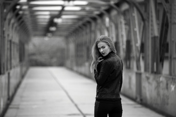 Obraz premium Beautiful blonde woman in leather jacket and leggings on a bridge