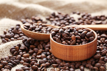 Coffee beans in wooden spoon and bowl on a sack, close up