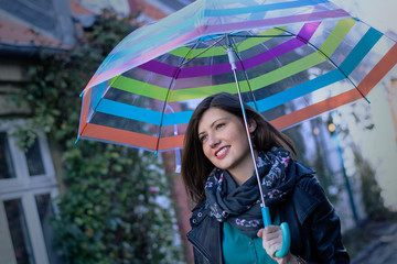 Smiling beautiful girl with her umbrella on a grey day. It is ra