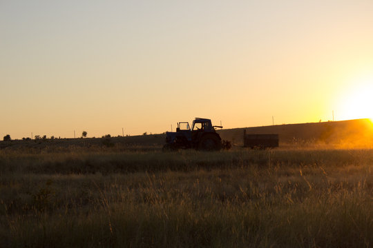 tractor rides at sunset, kicking up dust