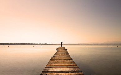 Man standing on a small jetty, enjoying the  sunset over a lake