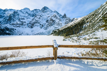 Wooden fence and view of frozen Morskie Oko lake in winter, Tatra Mountains, Poland