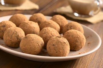 Homemade rum balls covered with cocoa powder, glass cups of hot chocolate in the back, photographed with natural light (Selective Focus, Focus on the two balls in the front)