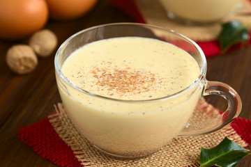 Eggnog drink in glass cup sprinkled with ground nutmeg, photographed on dark wood with natural light (Selective Focus, Focus one third into the eggnog)