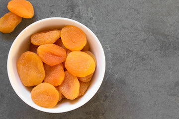 Dried apricots, a healthy snack containing vitamins, beta-carotene, fiber, antioxidants, photographed overhead on slate with natural light (Selective Focus, Focus on the apricots on the top)