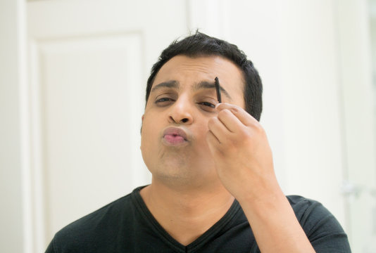 Closeup portrait, young handsome egotistical man in black t-shirt looking at mirror showing kisses and duck face, combing eyebrows admiring his appearance inside indoors background