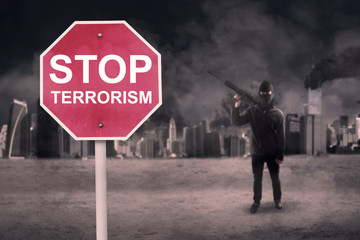 Road sign with text stop terrorism and man with rifle damaged city in background
