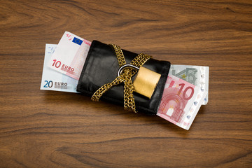 Euro banknotes in a locked wallet with golden chain and padlock.