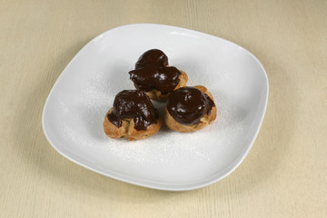 Profiteroles with chocolate icing on a plate with powdered sugar