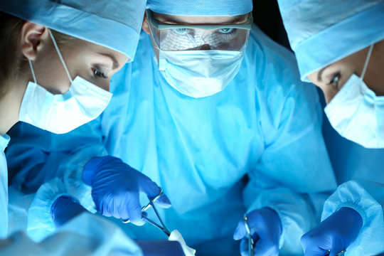 Three surgeons at work operating in surgical theatre