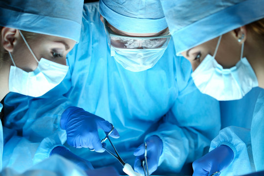 Three surgeons at work operating in surgical theatre