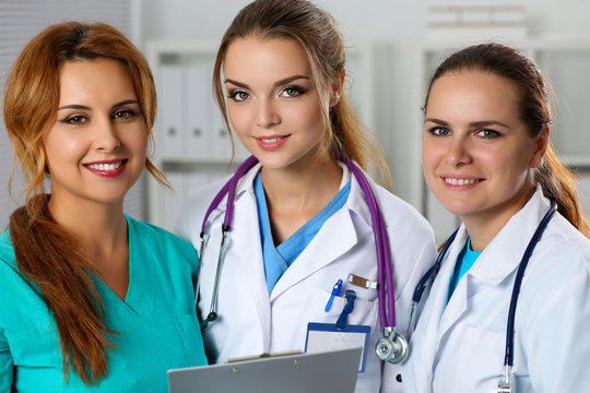 Three smiling female medicine doctors in office looking in camer