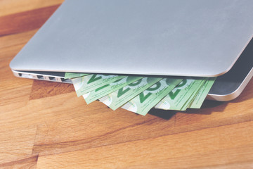 An image of pile of cash coming out from the laptop. Image has a light vintage effect applied.