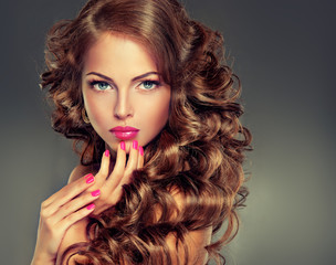 Beautiful model brunette with long curled hair . Hairstyle wavy curls . Crimson nails  manicure...