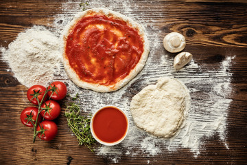 Pizza dough with ingredients on wood