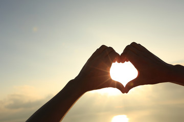 Heart shape making of hands against bright sea sunrise and sunny golden way at water