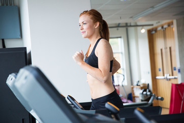 Fototapeta na wymiar Pretty woman with red hair running on treadmill in gym