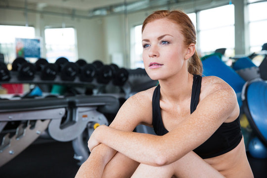 Pretty woman with red hair and freckles sitting in gym looking f
