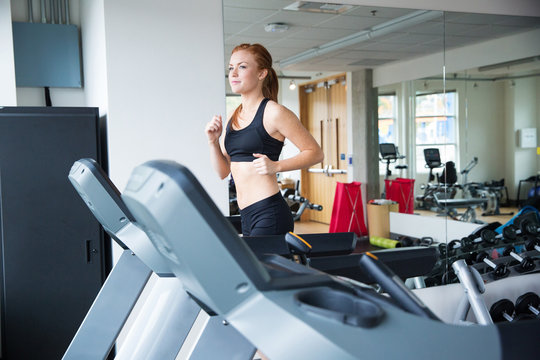 Pretty woman with red hair running on treadmill in gym