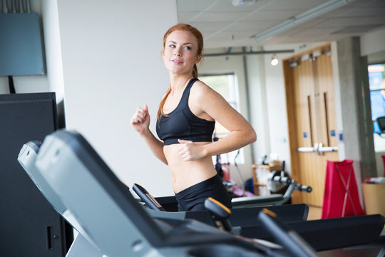 Pretty woman with red hair running on treadmill in gym