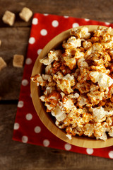 Sweet caramel popcorn in a bowl on red cotton napkin against wooden background