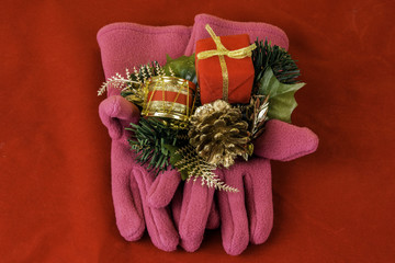 pair of pink gloves holding small wrapped gift drum garland and pine cone on red background