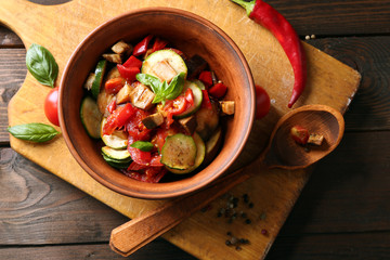 Tasty vegetarian ratatouille made of eggplants, squash, tomatoes in bowl on wooden table background