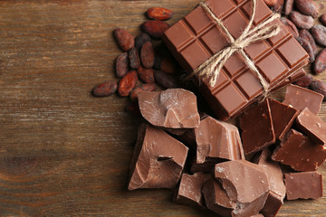 Chocolate pieces, shavings and cocoa beans on color wooden background
