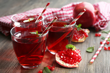 Three glasses of tasty juice and garnet fruit, on wooden background