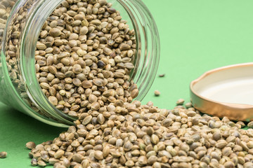 Obraz premium Close up of overturned glass jar with hemp seeds on a light green background with the lid next to it