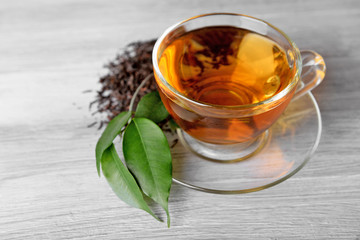 Glass cup of black tea with green leaves on grey wooden background