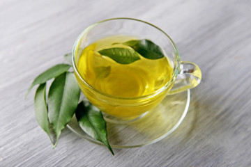 Glass cup of tea with green leaves on grey wooden background