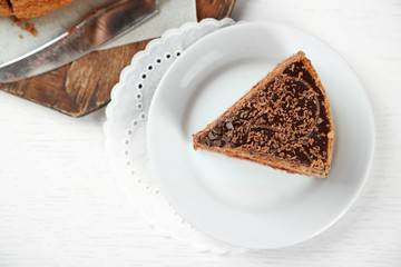 Sliced chocolate cake on wooden table, on light background