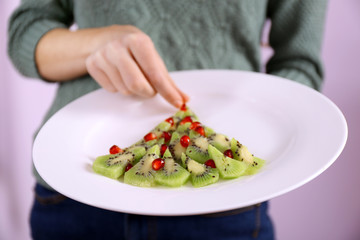 Woman holding plate with Christmas fir tree made from kiwi