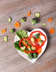 Useful cut vegetables on a plate in the form of heart on wooden table top view