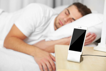 Beautiful young man waking up with mobile alarm clock
