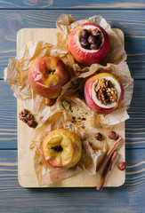 Baked apples with cinnamon sticks and hazelnuts on parchment paper and cutting board on wooden background top view