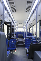 Bus inside, city transportation white interior with blue seats in row, retirement places, open doors, handles for standing passengers, bright lights and air conditioner 