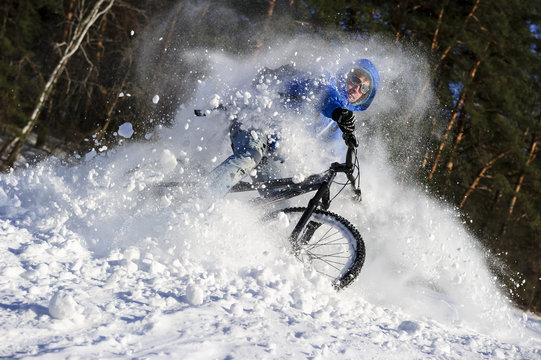 Extreme cyclist riding mountain bike in flying snow near winter forest in sunny cold day 