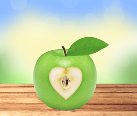 Fresh green apple with heart on wooden table over nature backgro