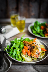 Chicken with potatoes and arugula salad on rustic background