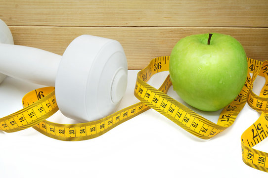 Time to Get Fit / An Apple, a Measure Tape and a Dumbbell on a Wooden Background