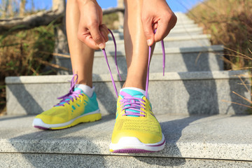 young woman runner tying shoelaces on stone trail