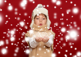 winter christmas concept - girl in hat and sweater blowing on pa