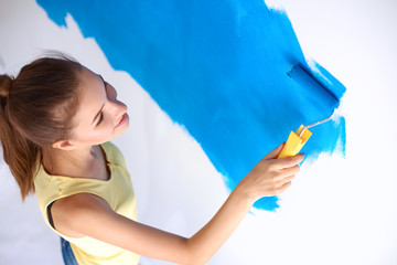 Happy beautiful young woman doing wall painting, standing on ladder