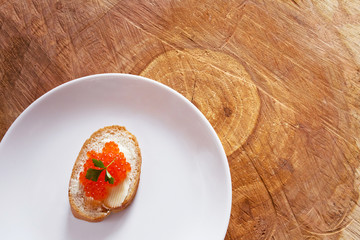Sandwich with red caviar on a plate on wooden background