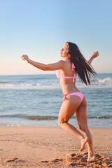Pretty girl in pink bikini dancing on sunny seaside beach